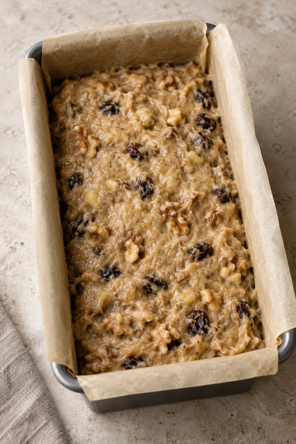 Banana batter with walnuts and raisins in a parchment-lined tin