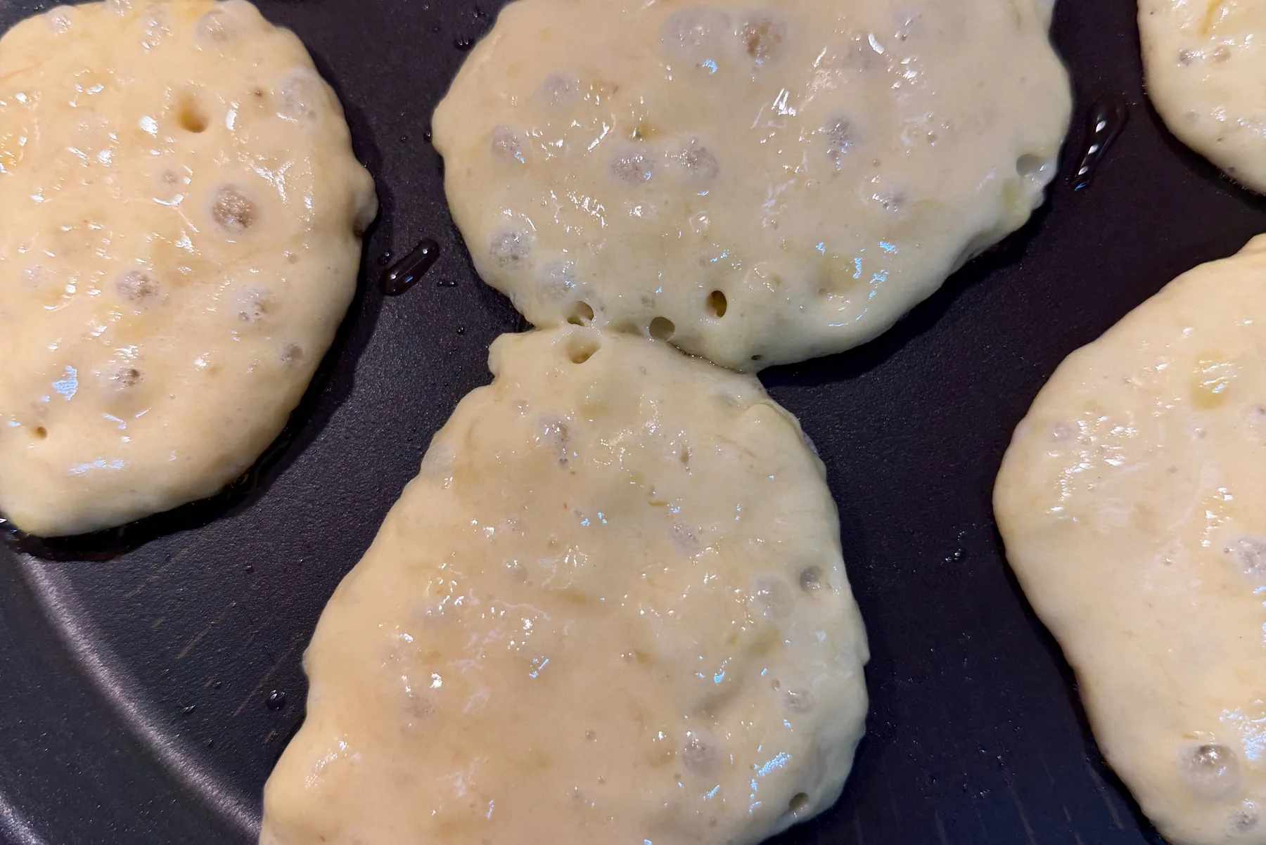 Homemade banana pancakes cooking on a pan as bubbles open on the surface