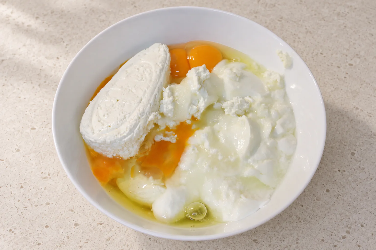 Tvorog curd cheese, eggs and natural yoghurt together in a white bowl before blending