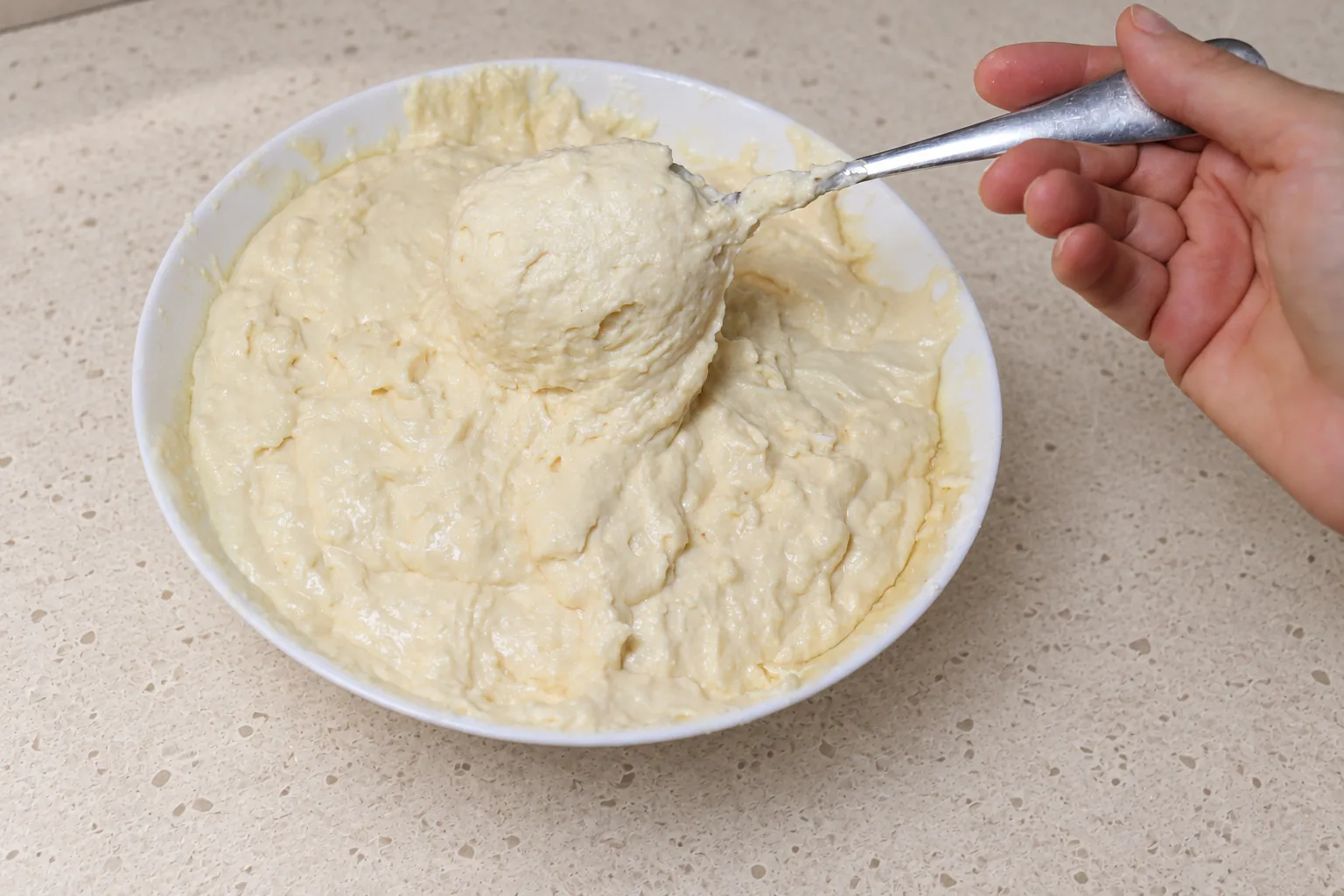 Thick, smooth waffle batter lifted on a spoon above the bowl