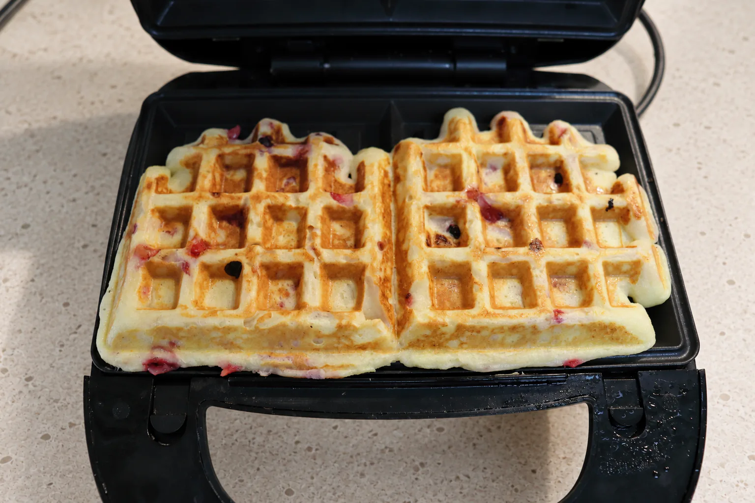 Two golden berry cottage-cheese waffles in an open waffle maker