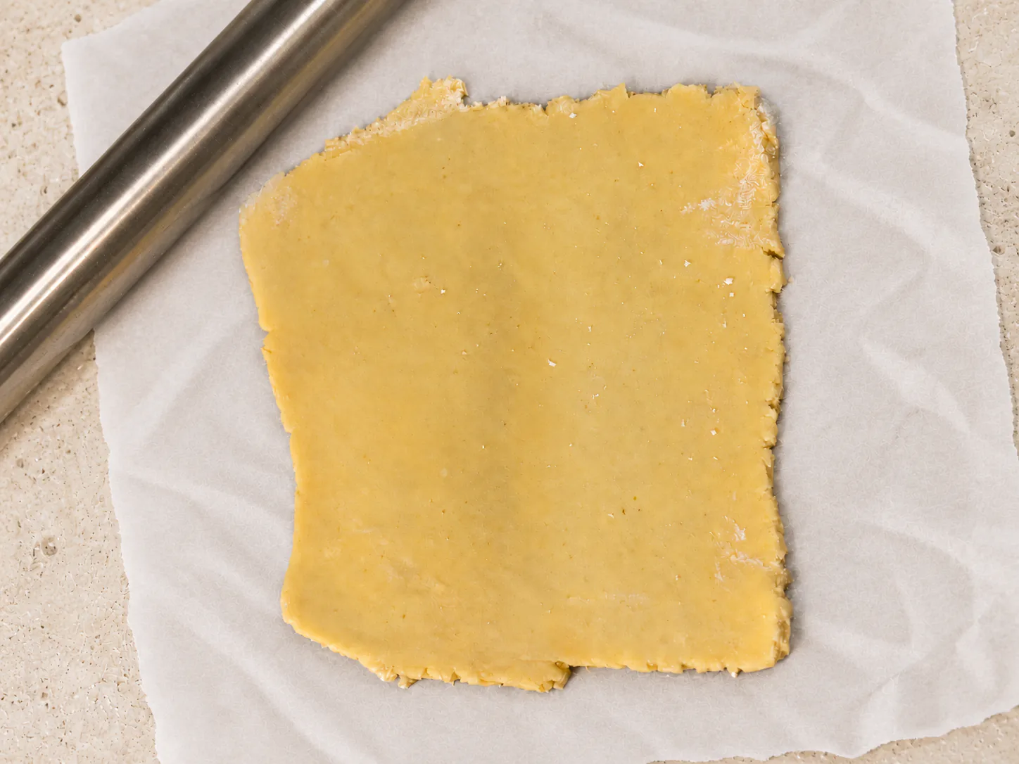 A portion of dough rolled into a square on parchment