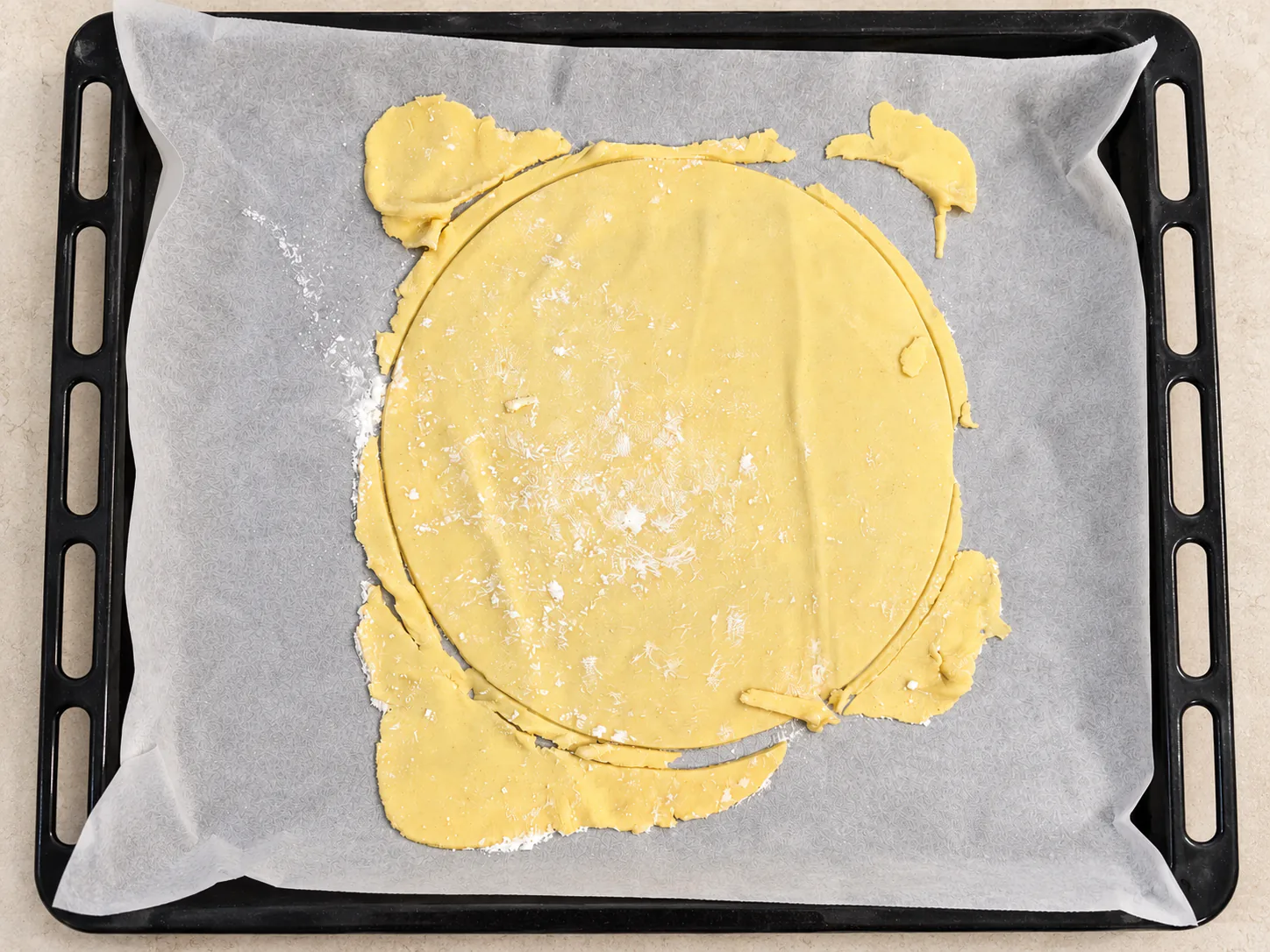 A round unbaked layer with trimmings on a parchment-lined tray