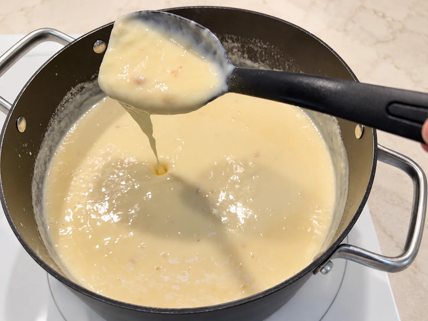 Thick custard flowing from a spoon into the saucepan