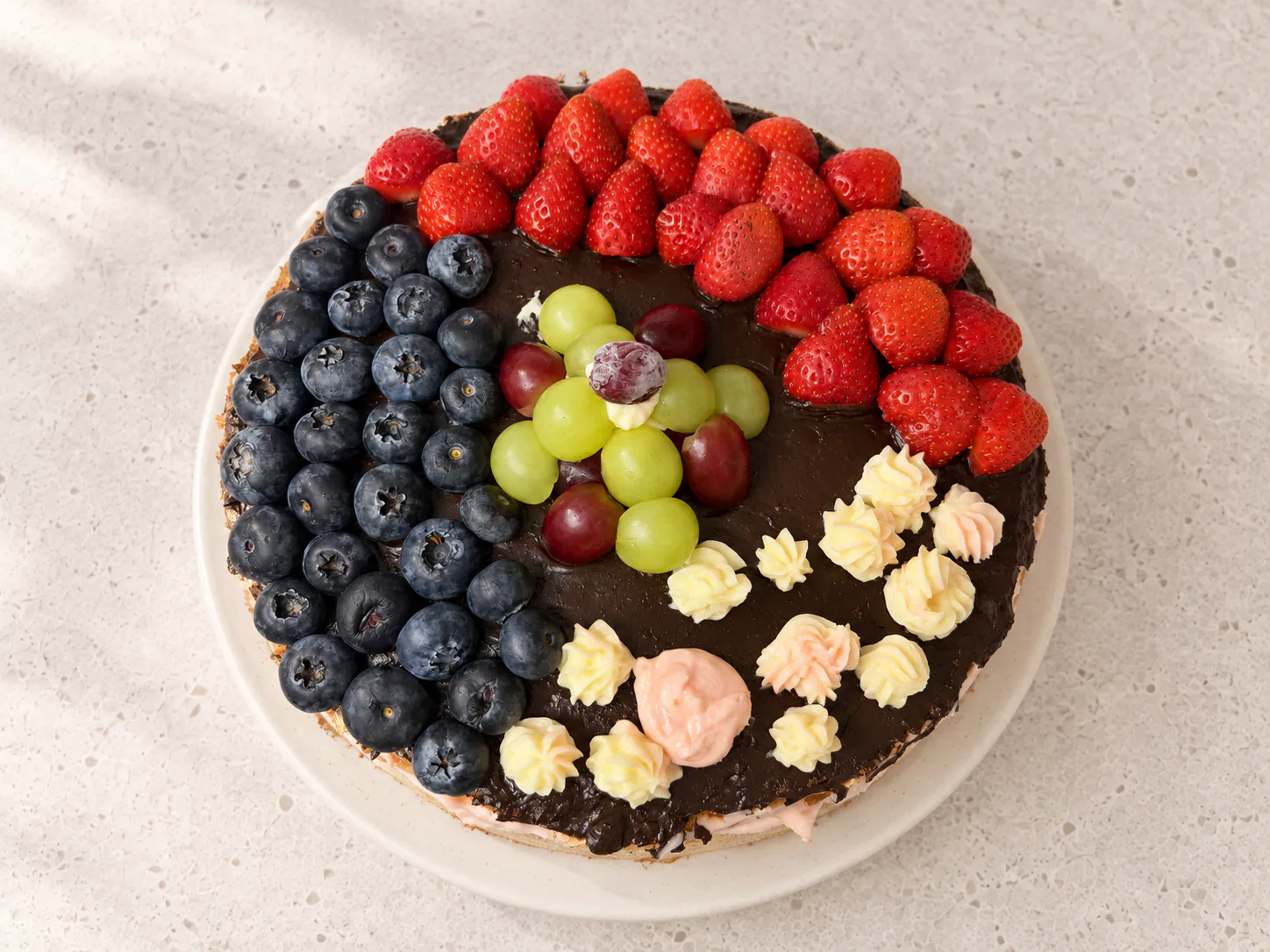 Cake with chocolate glaze, strawberries, blueberries, grapes and piped flowers